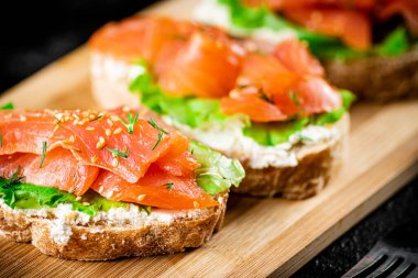 Sandwich with pieces of salmon on a cutting board. On a black background. High quality photo