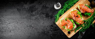 Sandwich with pieces of salmon on a cutting board. On a black background. High quality photo