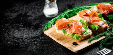 Sandwich with pieces of salmon on a cutting board. On a black background. High quality photo