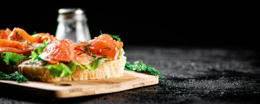 Sandwich with pieces of salmon on a cutting board. On a black background. High quality photo