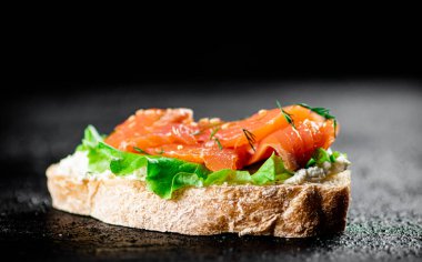 A flavorful salmon sandwich on the table. On a black background. High quality photo