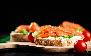 Sandwich with pieces of salmon on a cutting board. On a black background. High quality photo