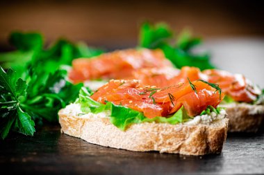 Sandwich with pieces of salmon and greens. Against a dark background. High quality photo