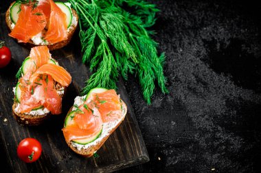 Salmon sandwich on a cutting board with herbs and tomatoes. On a black background. High quality photo