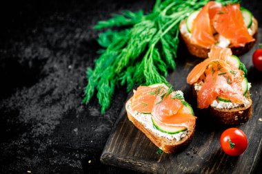 Salmon sandwich on a cutting board with herbs and tomatoes. On a black background. High quality photo