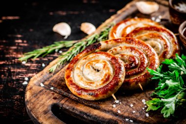 Grilled sausages on a cutting board with parsley and rosemary. On a rustic dark background. High quality photo