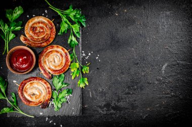 Grilled sausages on a stone board with tomato sauce and parsley. On a black background. High quality photo