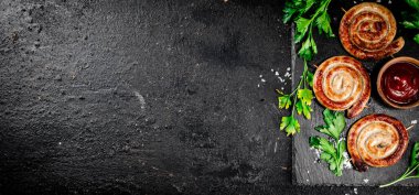 Grilled sausages on a stone board with tomato sauce and parsley. On a black background. High quality photo