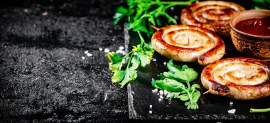 Grilled sausages on a stone board with tomato sauce and parsley. On a black background. High quality photo