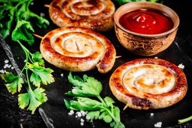 Grilled sausages on a stone board with tomato sauce and parsley. On a black background. High quality photo