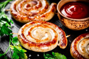 Grilled sausages on a stone board with tomato sauce and parsley. On a black background. High quality photo