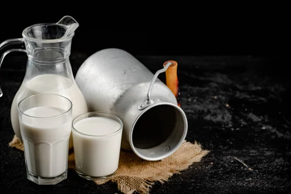 Rustic milk in a can and a glass on the table. On a black background. High quality photo
