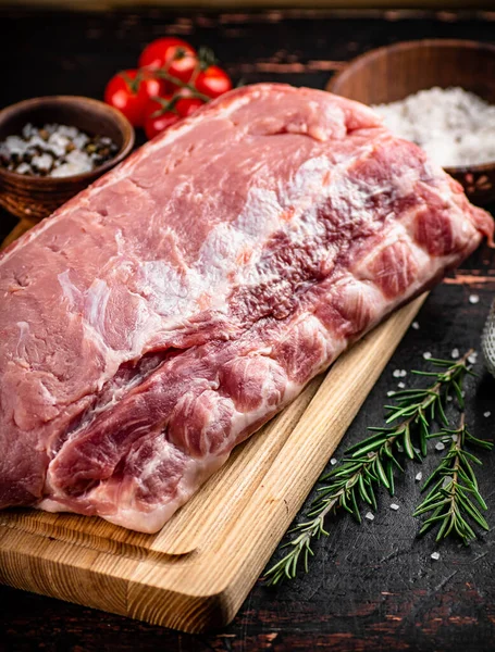 A piece of raw pork on a cutting board with tomatoes, spices and rosemary. On a rustic dark background. High quality photo