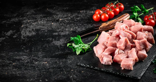 Pieces of raw pork on a stone board with parsley, tomatoes and spices. On a black background. High quality photo