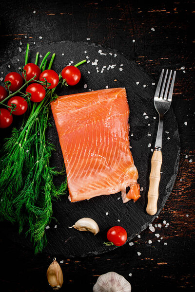 A piece of salted salmon with tomatoes and greens on a stone board. On a rustic with a dark background. High quality photo