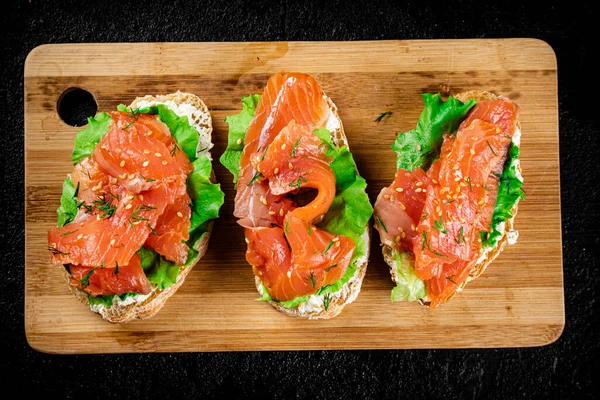 Sandwich with pieces of salmon on a cutting board. On a black background. High quality photo