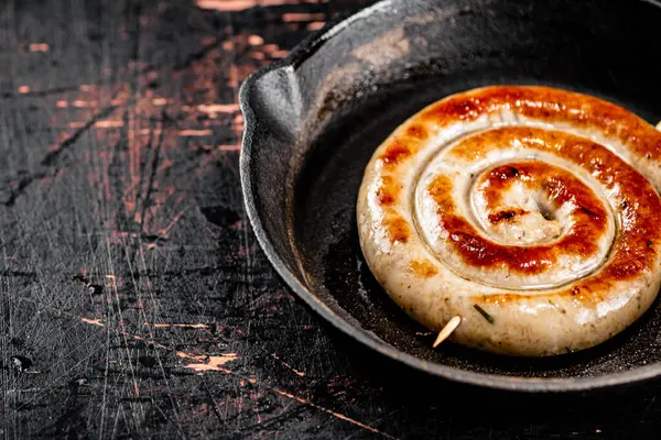 Delicious grilled sausage in a frying pan. Against a dark background. High quality photo