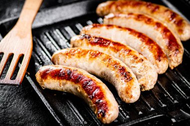 Grilled sausages in a frying pan with a wooden spatula. On a black background. High quality photo