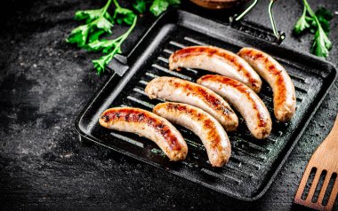 Grilled sausages in a frying pan with parsley. On a black background. High quality photo