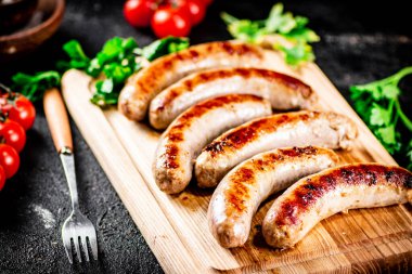 Grilled sausages on a wooden cutting board with parsley and tomatoes. On a black background. High quality photo