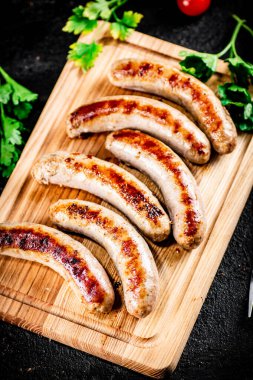 Aromatic grilled sausages on a cutting board. On a black background. High quality photo