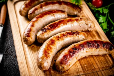 Grilled sausages on a wooden cutting board with parsley and tomatoes. On a black background. High quality photo