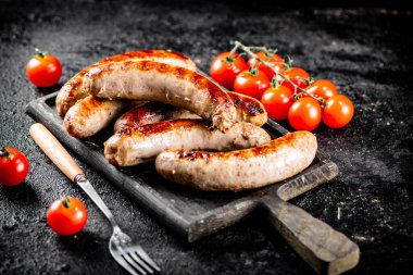 Grilled sausages on a cutting board with tomatoes. On a black background. High quality photo