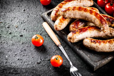 Grilled sausages on a cutting board with tomatoes. On a black background. High quality photo