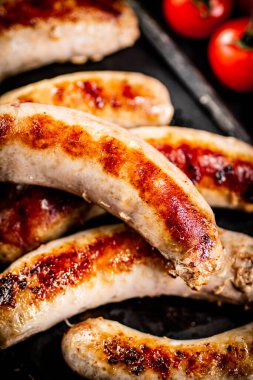 Grilled sausages on a cutting board with tomatoes. On a black background. High quality photo