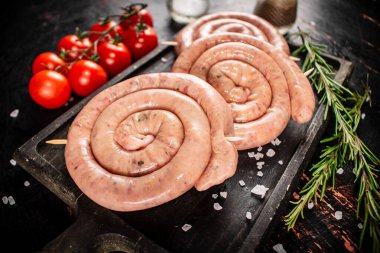 Raw sausages on a cutting board with a sprig of rosemary and tomatoes. On a rustic dark background. High quality photo