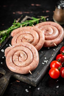 Raw sausages on a cutting board with a sprig of rosemary and tomatoes. On a rustic dark background. High quality photo