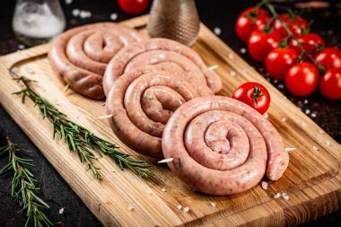 Raw sausages on a cutting board with a sprig of rosemary and tomatoes. On a rustic dark background. High quality photo