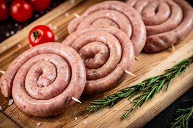 Raw sausages on a cutting board with a sprig of rosemary and tomatoes. On a rustic dark background. High quality photo