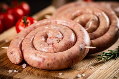 Raw sausages on a cutting board with a sprig of rosemary and tomatoes. On a rustic dark background. High quality photo