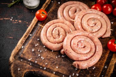 Raw sausages on a wooden cutting board with tomatoes. On a rustic background. High quality photo