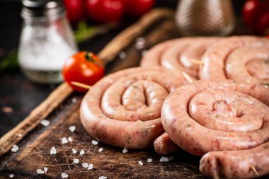 Raw sausages on a wooden cutting board with tomatoes. On a rustic background. High quality photo