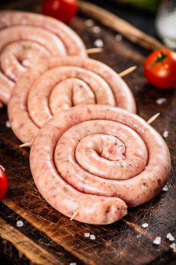 Raw sausages on a wooden cutting board with tomatoes. On a rustic background. High quality photo