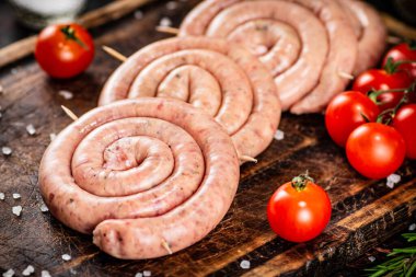 Raw sausages on a wooden cutting board with tomatoes. On a rustic background. High quality photo