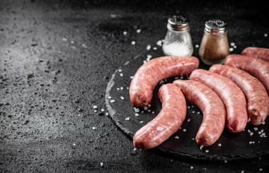 Raw sausages on a stone board with spices. On a black background. High quality photo