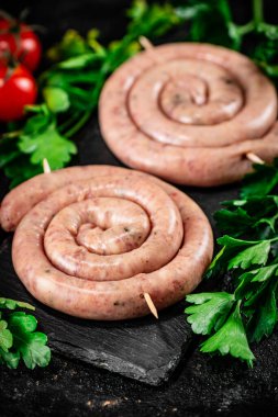 Raw sausages on a stone board with parsley and tomatoes. On a black background. High quality photo