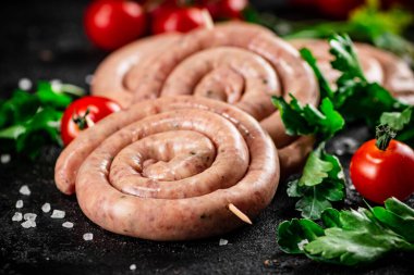 Round raw sausages with tomatoes and parsley. On a black background. High quality photo