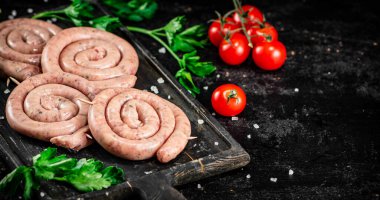 Raw sausages with parsley and tomatoes. On a black background. High quality photo