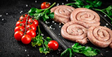 Raw sausages with parsley and tomatoes. On a black background. High quality photo