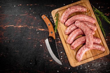 Raw sausages on a cutting board with a knife and rosemary. Against a dark background. High quality photo