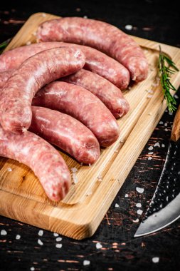 Raw sausages on a cutting board with a knife and rosemary. Against a dark background. High quality photo