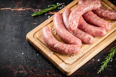 Raw sausages on a cutting board with a sprig of rosemary. On a rustic dark background. High quality photo