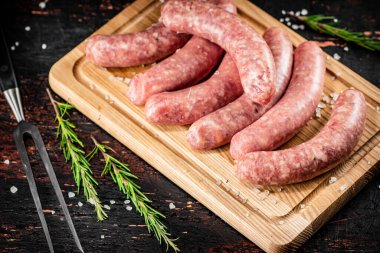 Raw sausages on a cutting board with a sprig of rosemary. On a rustic dark background. High quality photo