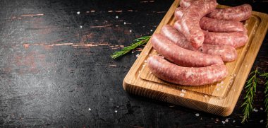 Raw sausages on a cutting board with a sprig of rosemary. On a rustic dark background. High quality photo