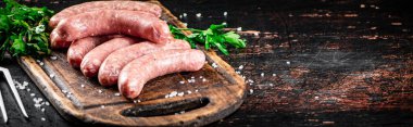 Raw sausages on a cutting board with parsley. On a rustic dark background. High quality photo