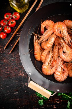 Cooked shrimp in a saucepan with parsley and tomatoes. On rustic dark background. High quality photo